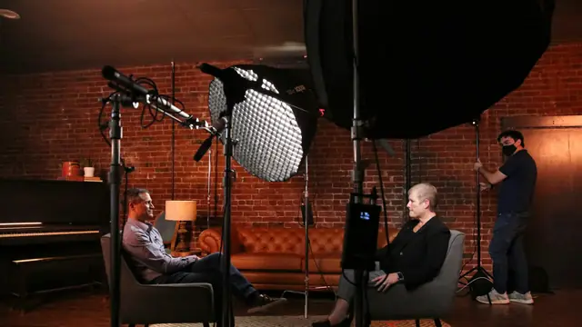 Two people seated for a lit interview in a brick-walled studio