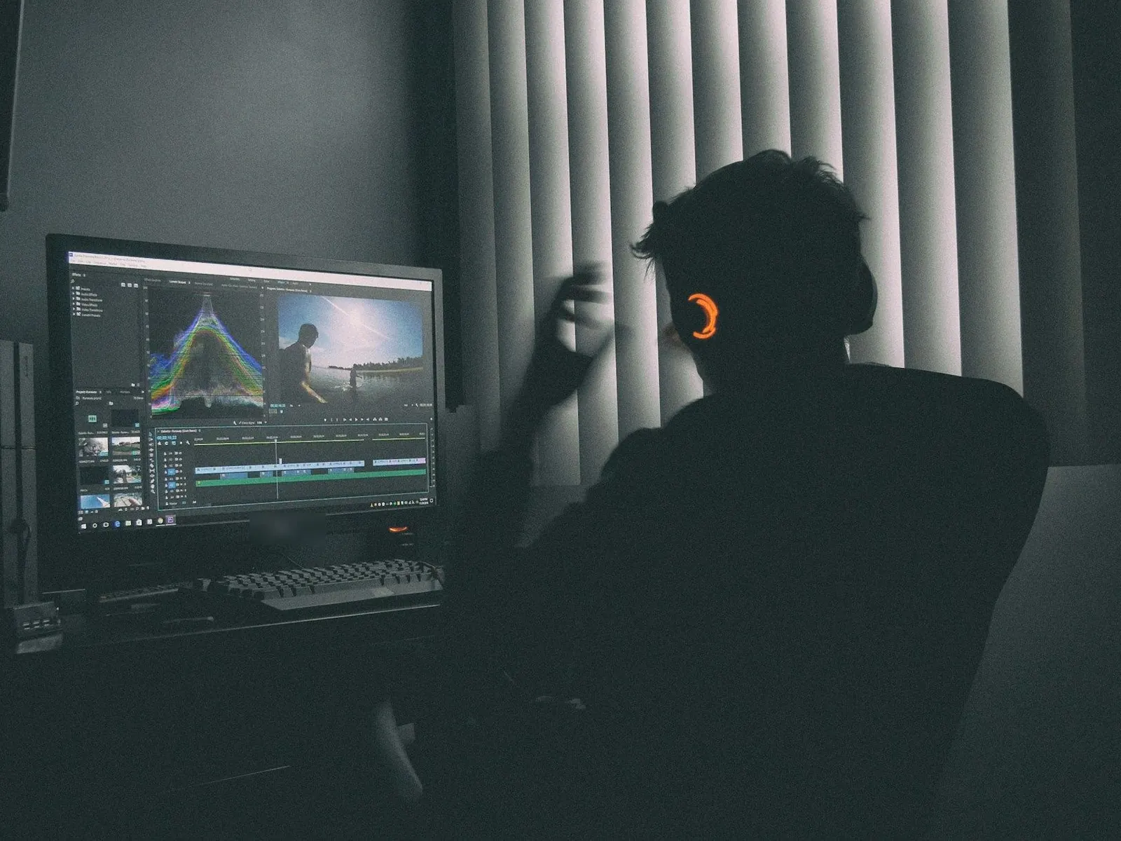 Video editor with headphones working at a monitor in a dark studio